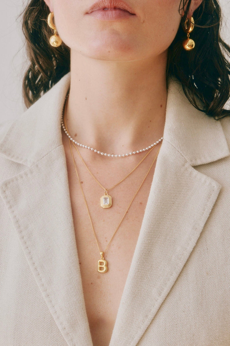 Woman wearing gold jewelry including earrings, necklaces, and a blazer.
