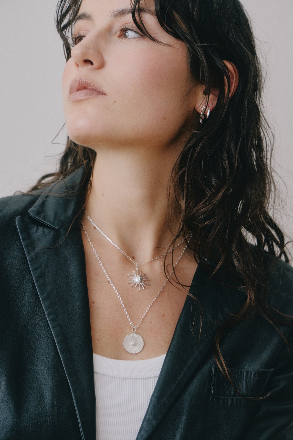 Layered silver necklaces with a sun pendant and a coin pendant